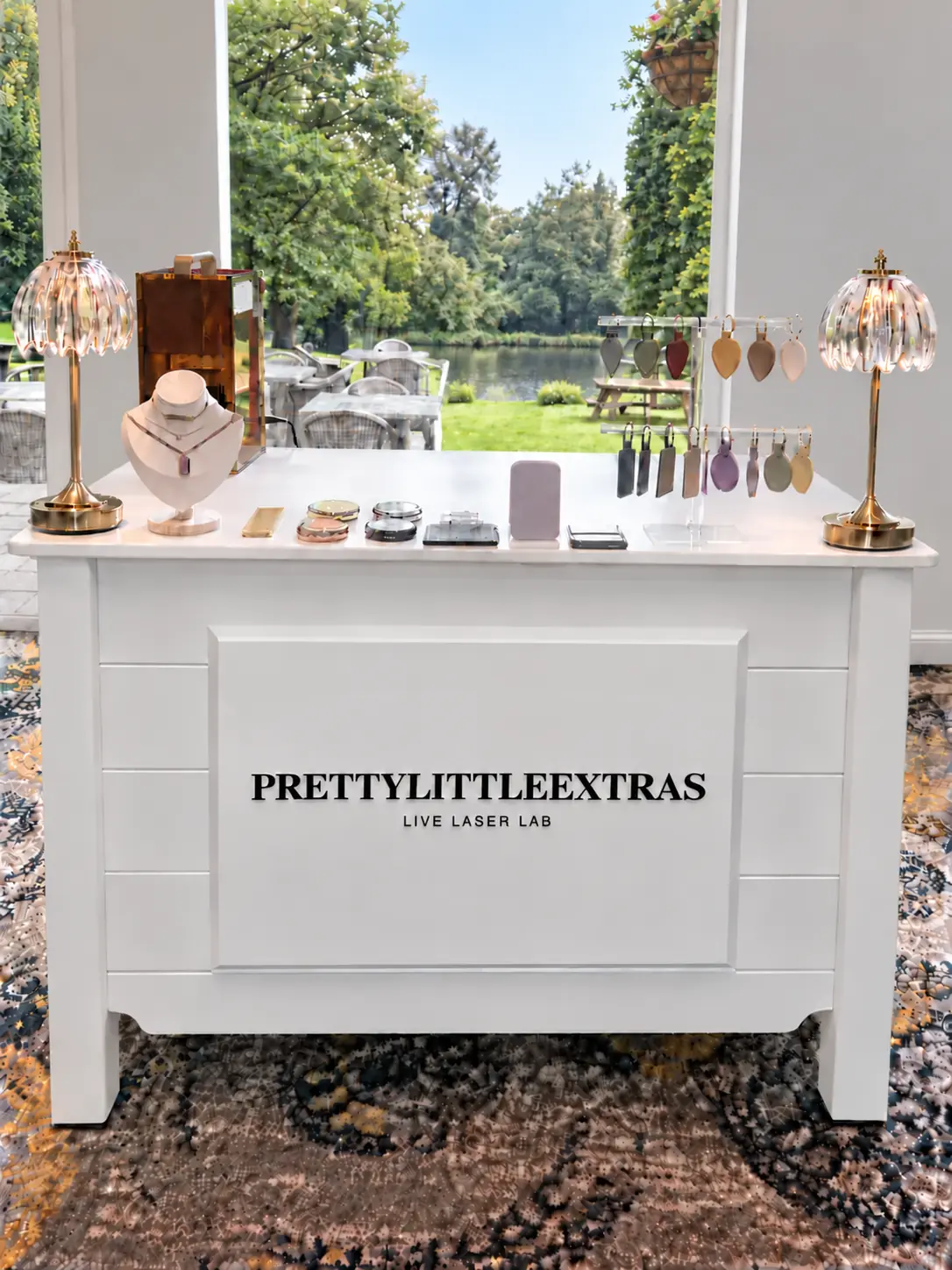 PrettyLittleExtras white Live Laser Lab event cart with acrylic displays, personalised keepsakes and an open garden view